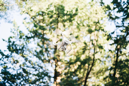 White quadcopter soars in the air against the background of trees in the park