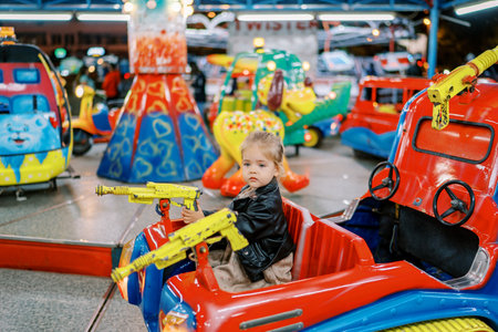 Little girl rides a toy tank on a carousel holding a steering wheelの写真素材