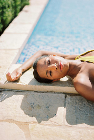 Young woman sunbathing lying on the edge of the pool with her hand behind her head