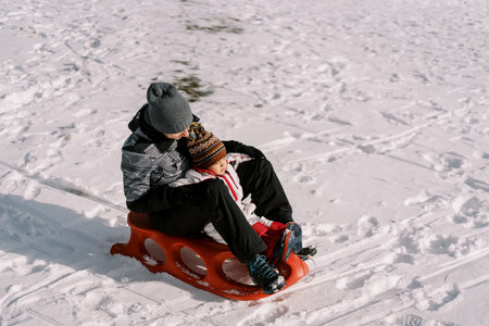 Mom with a small child are sitting on a sleigh on a snowy plainの写真素材