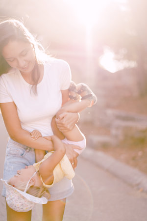 Smiling mom holding little girl upside down in bright sunlightの写真素材
