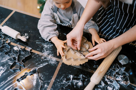 Little girl looks at her mother placing cookie cutters on the dough on the table. Top viewの写真素材