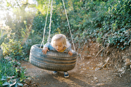 Little girl swings on a tire swing, leaning on her belly