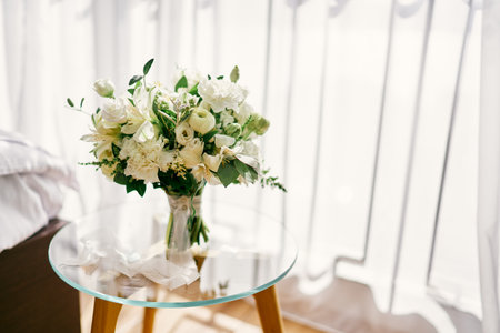 Wedding bouquet stands on a glass table in a room against the background of a white curtainの写真素材