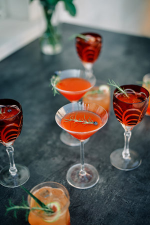 Glasses with red cocktails decorated with green twigs and berries stand on the table