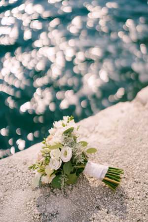 Bridal bouquet lies on a stone border near the shining waterの写真素材