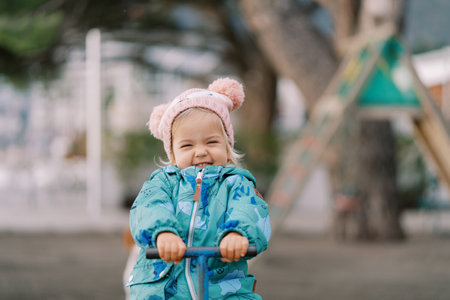 Smiling little girl sits on a swing, holding the handleの写真素材