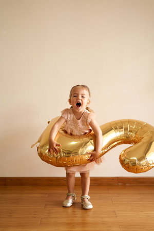 Little laughing girl with a number two in front of her stands against the wall