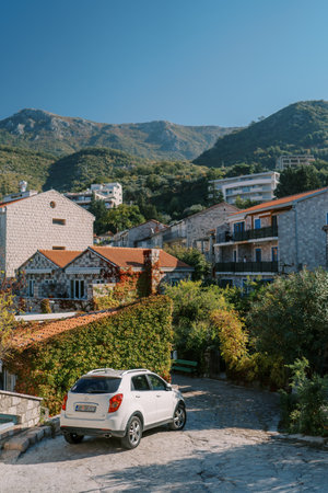Car stands near a hedge near cozy apartment buildings at the foot of the mountainsの写真素材