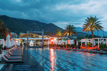 Red lighting by the long pool with a square arch and sun loungers at the foot of the mountains. Porto, Montenegroの写真素材
