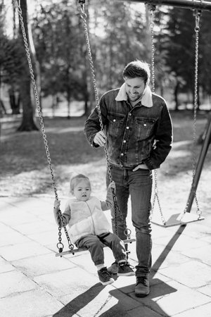 Smiling dad swings a little girl on a chain swing in the park. Black and white photoの写真素材