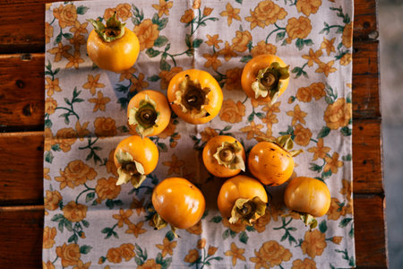 Ripe persimmons are laid out on a colorful tablecloth on a wooden table. Top viewの写真素材