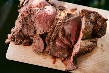 Roast beef cut into thin slices lies on a wooden board on the table in the sunの写真素材