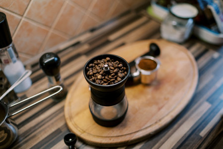 Coffee beans are poured into a manual coffee grinder standing on a wooden tray on the tableの写真素材