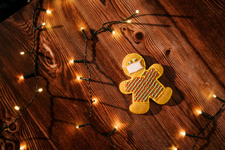 Cookie in a mask lies on a table with luminous garlands. Top view