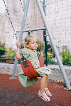 Little girl swings on a chain swing at the playground