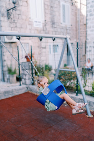Little girl swings on a chain swing in the courtyard of an old house
