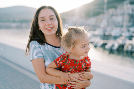 Smiling mother with a little girl in her arms stands on the boardwalk