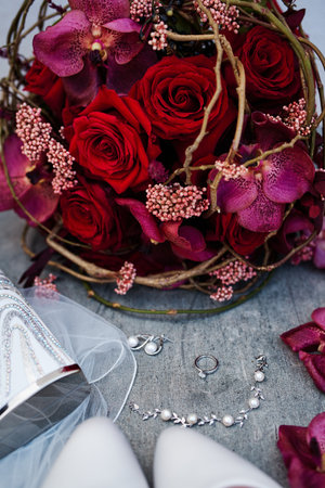 Earrings, bracelet and wedding ring lie near the bride bouquet on a wooden tableの写真素材