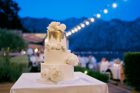 Three-tier wedding cake stands on a table in an evening garden with illuminationの写真素材