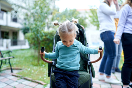 Little girl gets down from her stroller unbuckling her safety belt in the garden