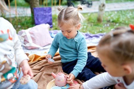 Little girls play tea ceremony while sitting on a blanket in the garden