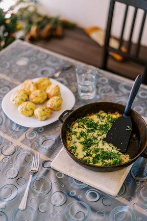 Frittata with herbs in a pan stands on the table next to the baked potatoes on the plateの写真素材