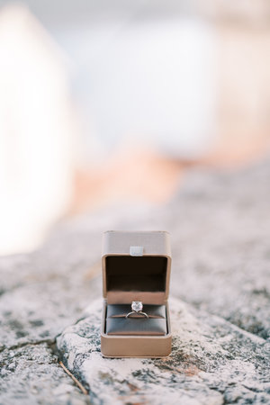 Engagement ring lies in an open box on a stone fence