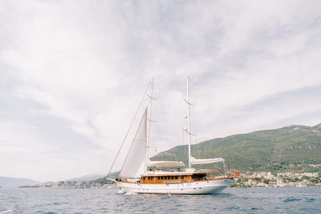 Luxury sailing yacht sails on the sea against the backdrop of green mountainsの写真素材