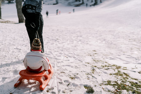 Mom carries a small child on a sled across a snowy plain. Back view. Croppedの写真素材
