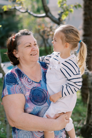 Little girl looking at smiling grandmother while sitting in her arms in the garden