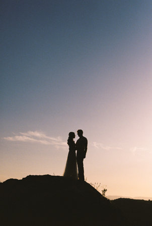 Silhouettes of bride and groom standing on the mountain at sunsetの写真素材