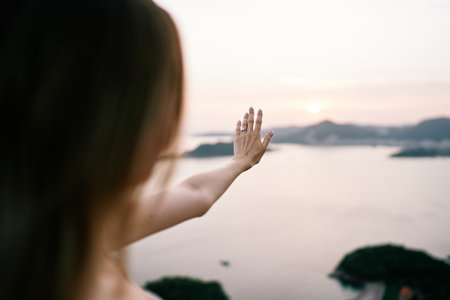 Girl examines her hand with a wedding ring against the background of the sky over the sea. Back viewの写真素材