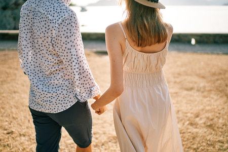 Man and woman walk along the seashore holding hands. Back view. Croppedの写真素材