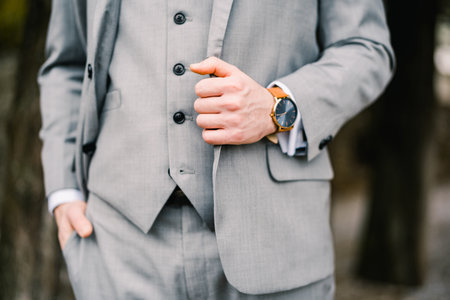 Man in a gray suit stands with one hand in his trouser pocket, and the other holding on to the lapel of his jacket. Cropped. Facelessの写真素材
