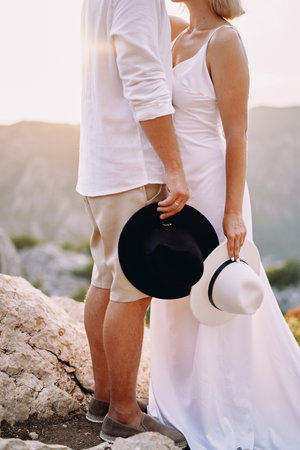 Groom and bride standing in the mountains with hats in their hands. Cropped. Facelessの写真素材