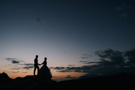 Silhouettes of bride and groom standing on the mountain at sunsetの写真素材