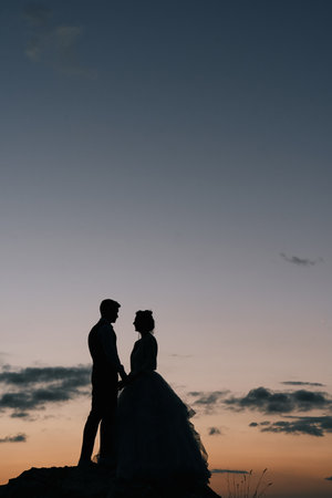 Bride and groom stand on the mountain holding hands at duskの写真素材