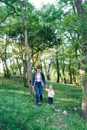 Mom with a little girl walks through the forest holding her handの写真素材