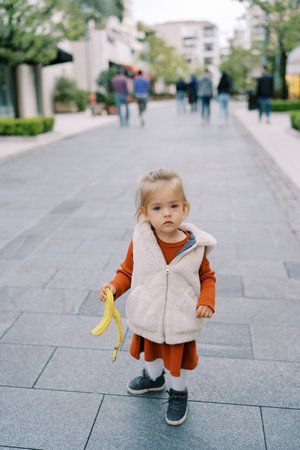 Little girl carries a banana down the streetの写真素材
