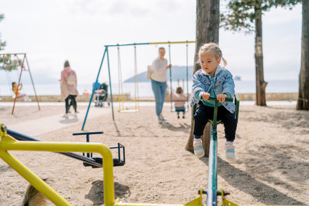 Little girl sits on a swing-balancer in the playground and looks downの写真素材
