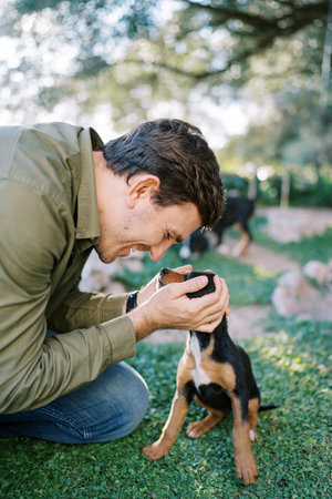 Smiling man leaning towards the puppy holding his head with his palmsの写真素材
