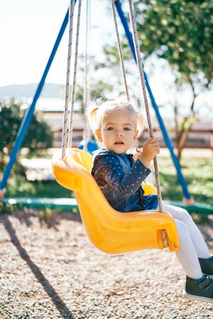 Little girl sits on a swing and looks awayの写真素材