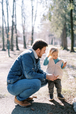 Dad is squatting near a little girl standing with a pinecone in her handの写真素材