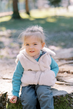Happy little girl sitting on stump in sunny parkの写真素材