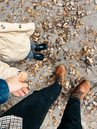 Man with a child stand on the pavement among fallen leaves. Top view