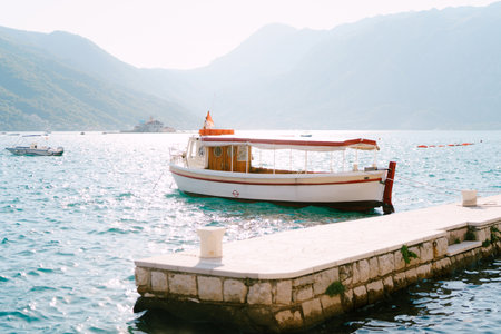 Excursion boat is moored to the bollard on the pier in the sea against the backdrop of the mountainsの写真素材