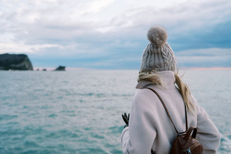 Girl with a backpack stands on the seashore and looks at the sunset. Back viewの写真素材