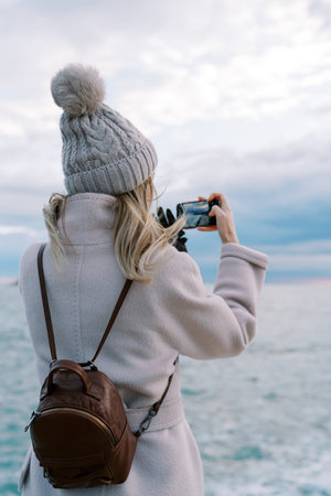 Girl stands on the seashore and photographs the horizon with a smartphone. Side viewの写真素材