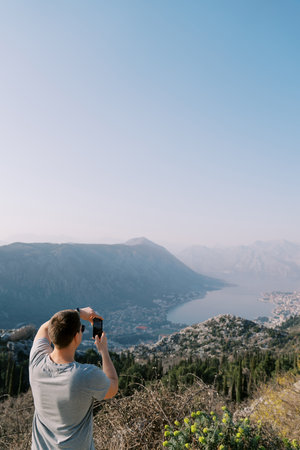Man stands on a mountain and photographs a view of the Bay of Kotor with a smartphone. Montenegro. Back viewの写真素材